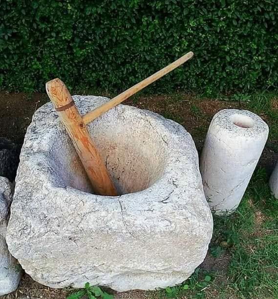 A large carved stone mortar with a wooden pestle resting in it, on grass
